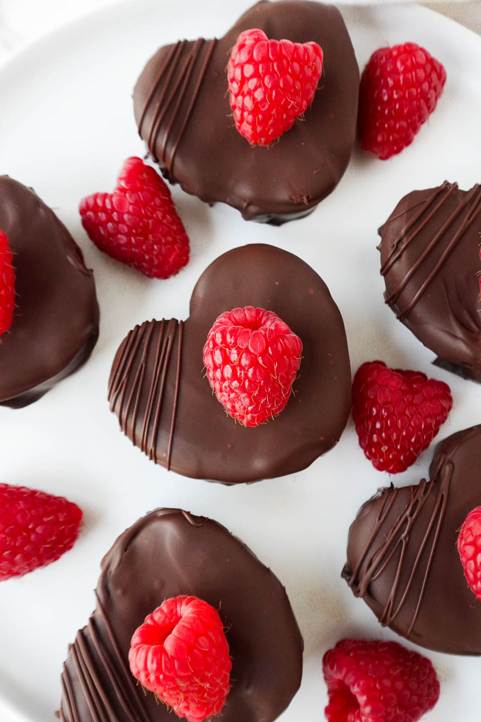 Heart-shaped no-bake raspberry brownies coated in dark chocolate, garnished with a fresh raspberry on top.