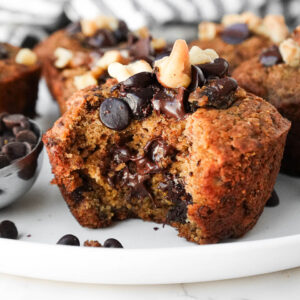 Moist and tender healthy banana muffins on a plate with a bite taken out showing gooey chocolate chips and it's fluffy, moist texture