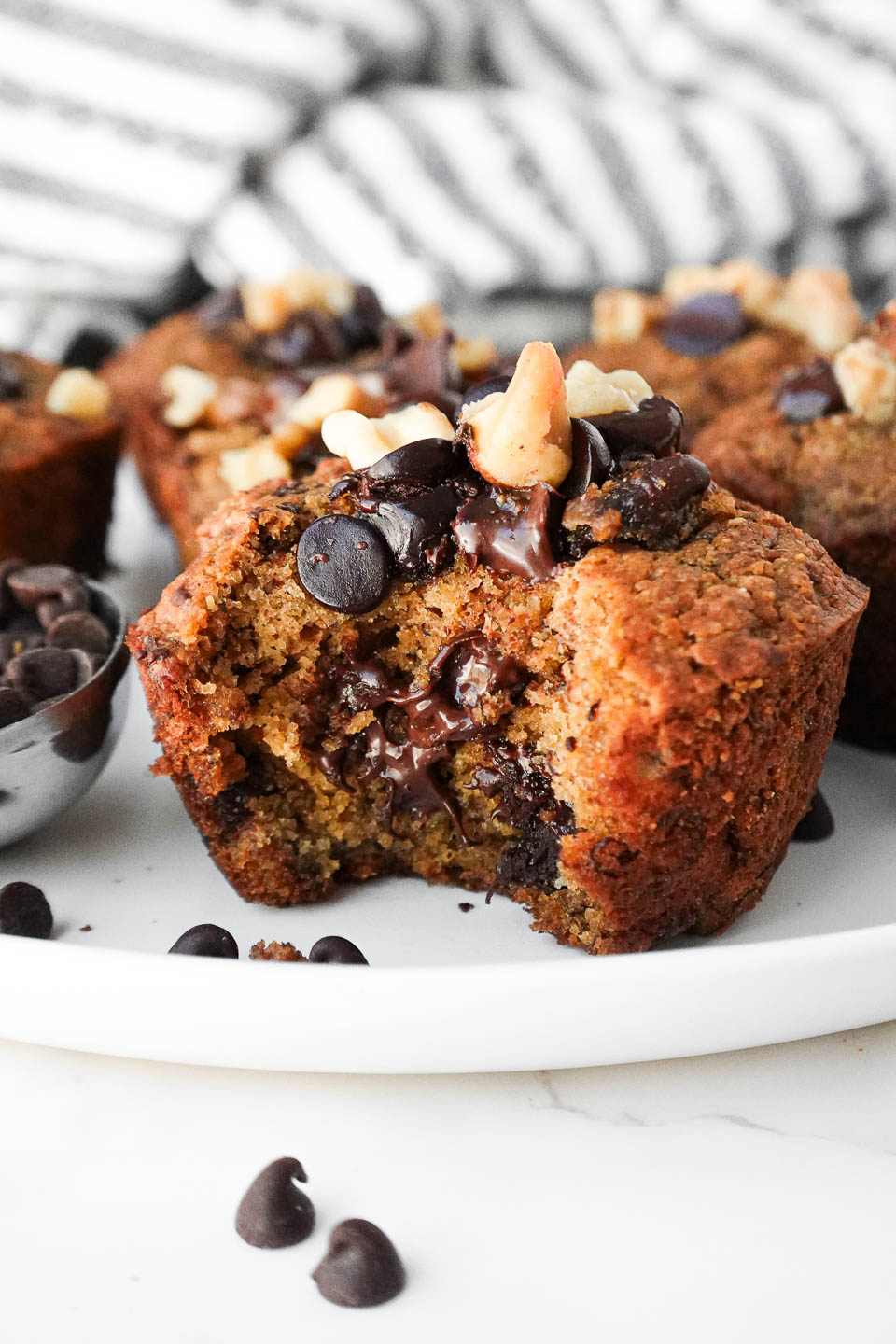 Moist and tender healthy banana muffins on a plate with a bite taken out showing gooey chocolate chips and it's fluffy, moist texture