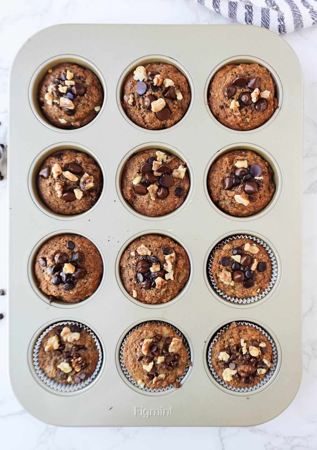 Freshly baked healthy banana muffins in a muffin tin, topped with chopped walnuts and chocolate chips