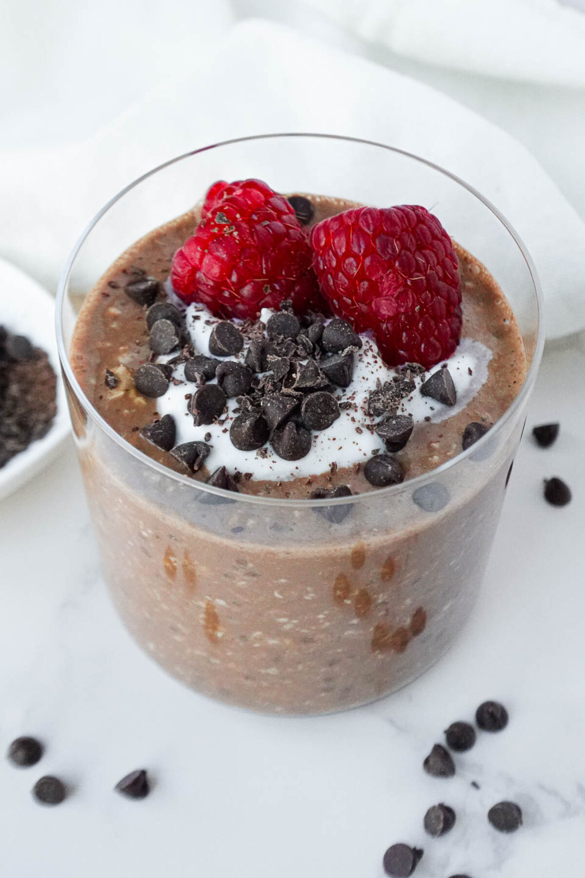 Decadent Brownie Batter Overnight Oats topped with vegan yogurt, chocolate chips and fresh raspberries.