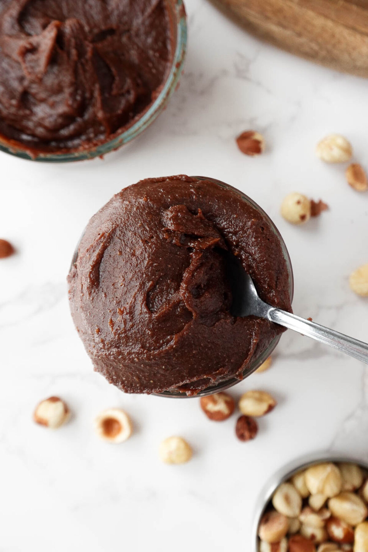 creamy homemade Nutella in a glass jar, surrounded by hazelnuts, vegan and naturally sweetened with dates
