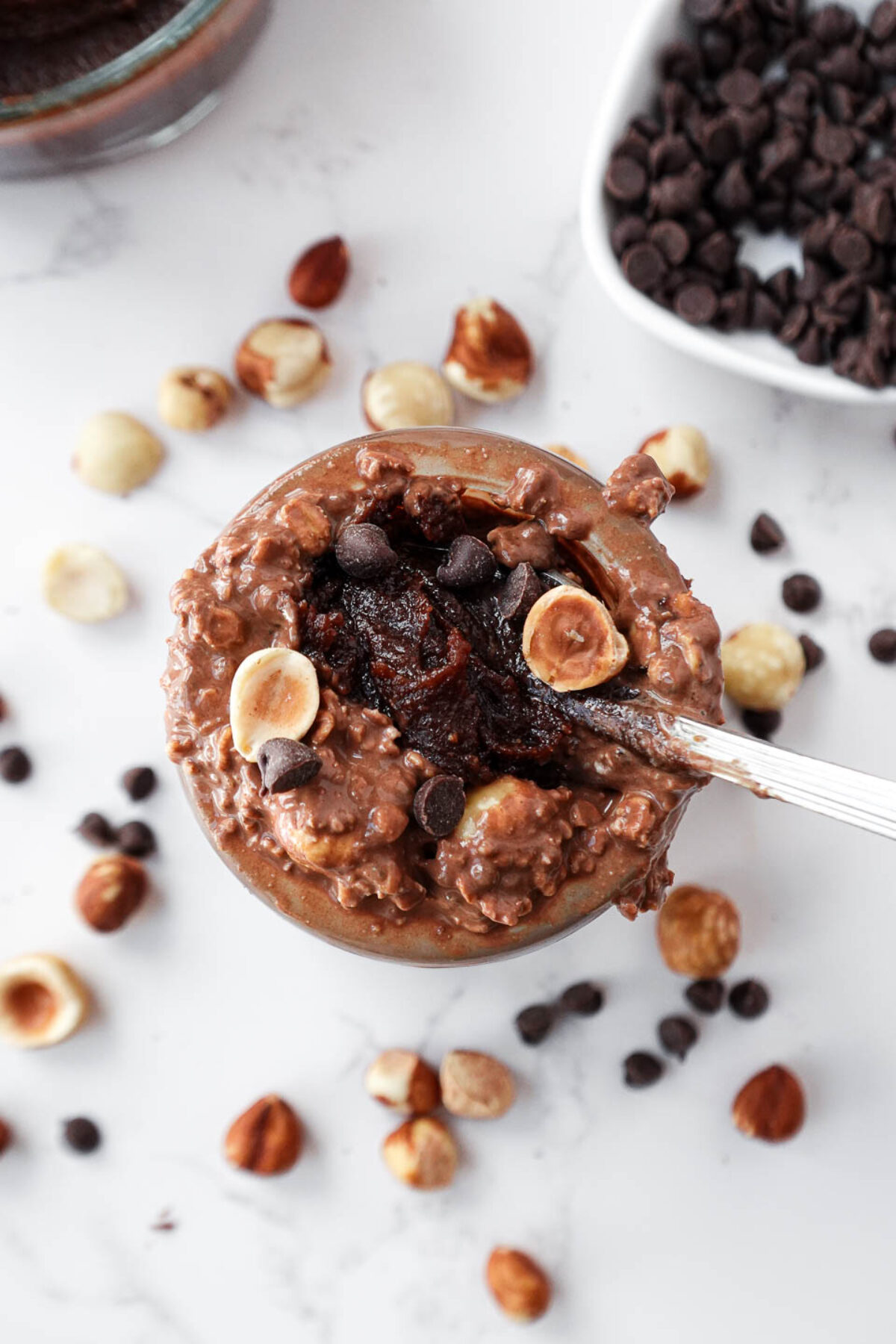 A spoon scooping up thick and creamy chocolate hazelnut overnight oats with dark chocolate chips and hazelnuts on top.