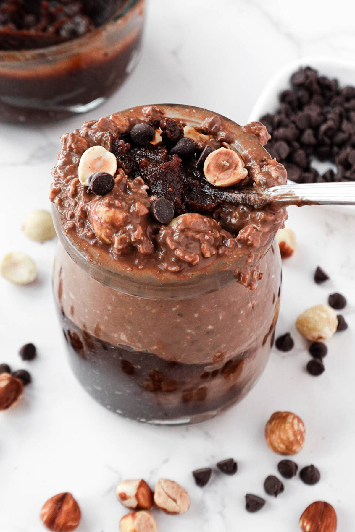 A glass jar filled with creamy chocolate hazelnut overnight oats, topped with chopped hazelnuts and a spoonful of homemade Nutella