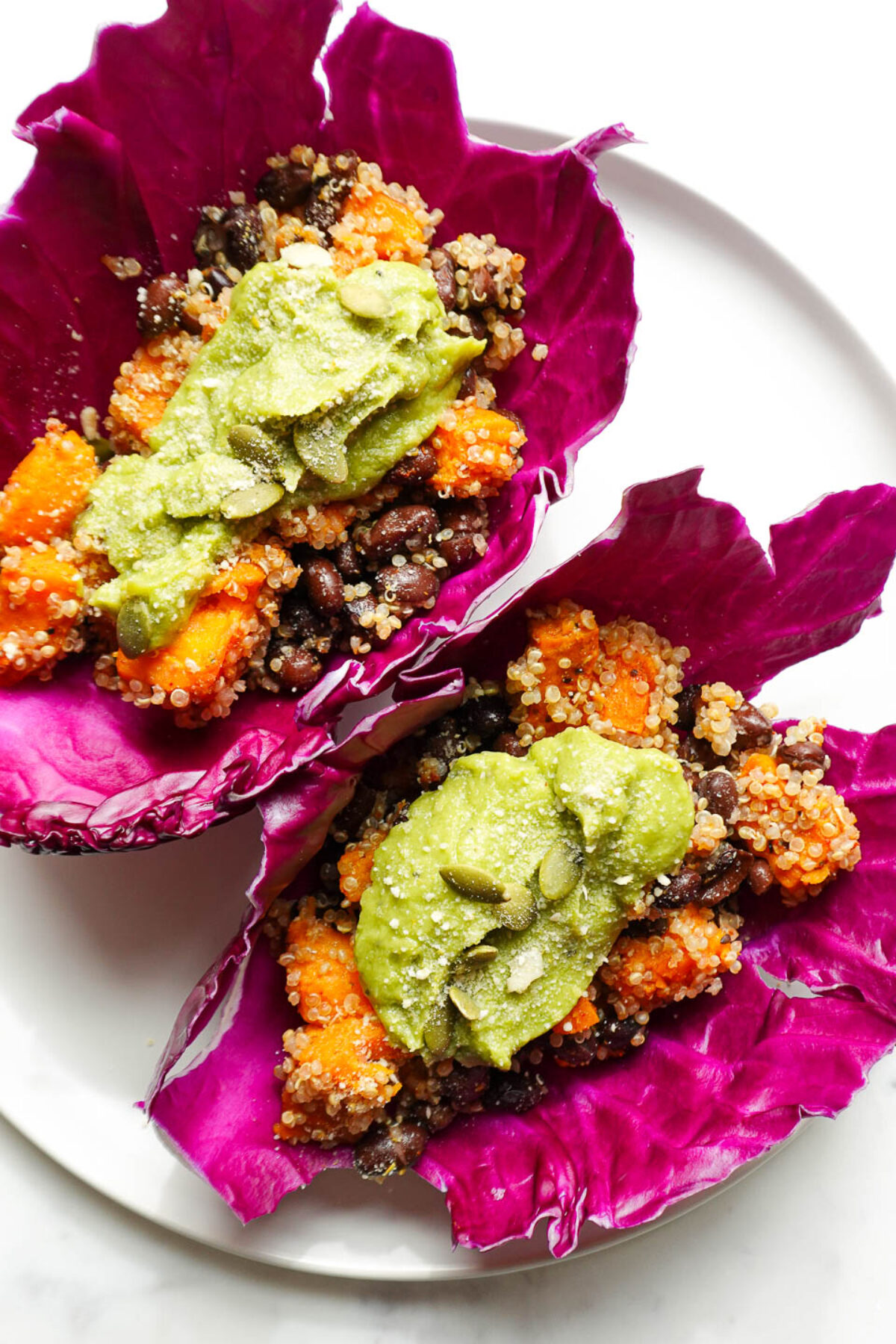 Vegan sweet potato and black bean tacos wrapped in vibrant red cabbage leaves, topped with guacamole