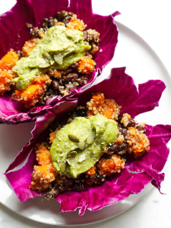 Close-up of hearty quinoa, roasted sweet potato, and black beans tacos wrapped in red cabbage leaves.
