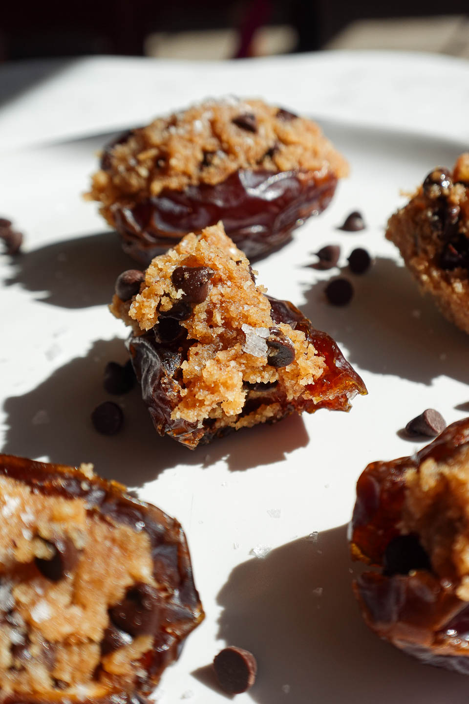 Bite taken out of a healthy and indulgent cookie dough stuffed date topped with chocolate and sea salt.