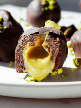 Pistachio stuffed date cut in half, showing creamy pistachio butter drizzling out, with a sprinkle of chopped pistachios on top.