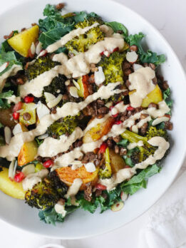 Roasted Potato & Lentil Buddha Bowl with crispy lentils, roasted broccoli, golden potatoes, sautéed kale, and topped with sliced almonds, pomegranate seeds, and a drizzle of creamy lemon tahini dressing.