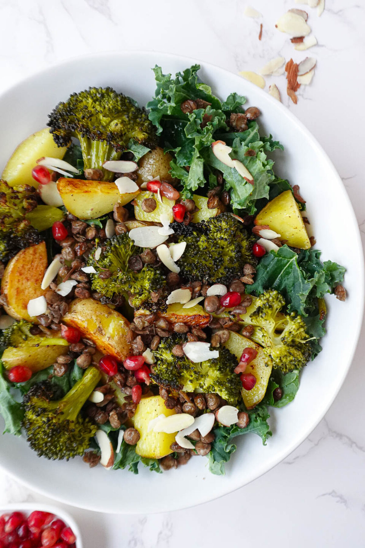 Healthy Roasted Potato & Lentil Buddha Bowl featuring golden potatoes, roasted broccoli, lentils, sautéed kale, and topped with pomegranate seeds, sliced almonds, and lemon tahini dressing.