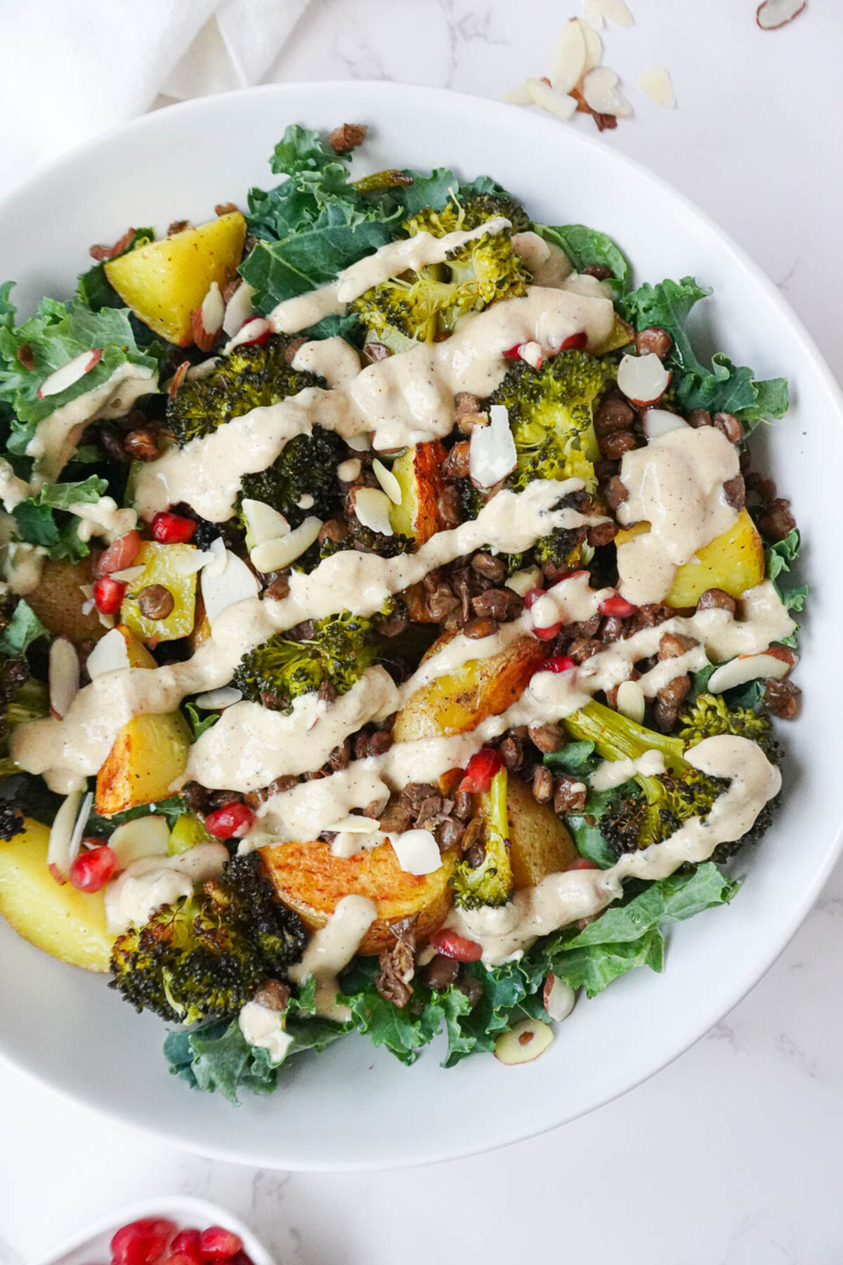 Delicious vegan Roasted Potato & Lentil Buddha Bowl with roasted vegetables, crispy lentils, and fresh kale, drizzled with creamy lemon tahini dressing and sprinkled with almonds and pomegranate seeds.