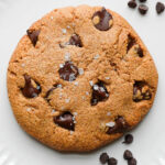 Single serve chocolate chip cookie with crisp edges and a soft, gooey center, topped with melty chocolate chips on a plate.