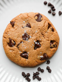Single serve chocolate chip cookie with crisp edges and a soft, gooey center, topped with melty chocolate chips on a plate.
