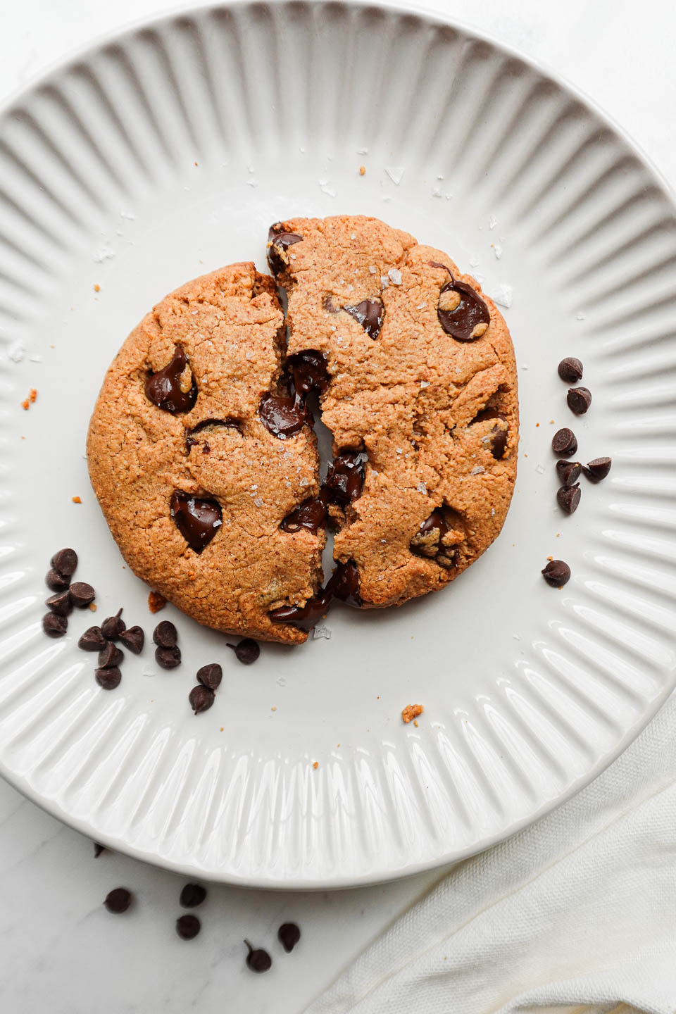 Melty chocolate dripping from the inside of a warm, soft-baked vegan and gluten-free chocolate chip cookie.