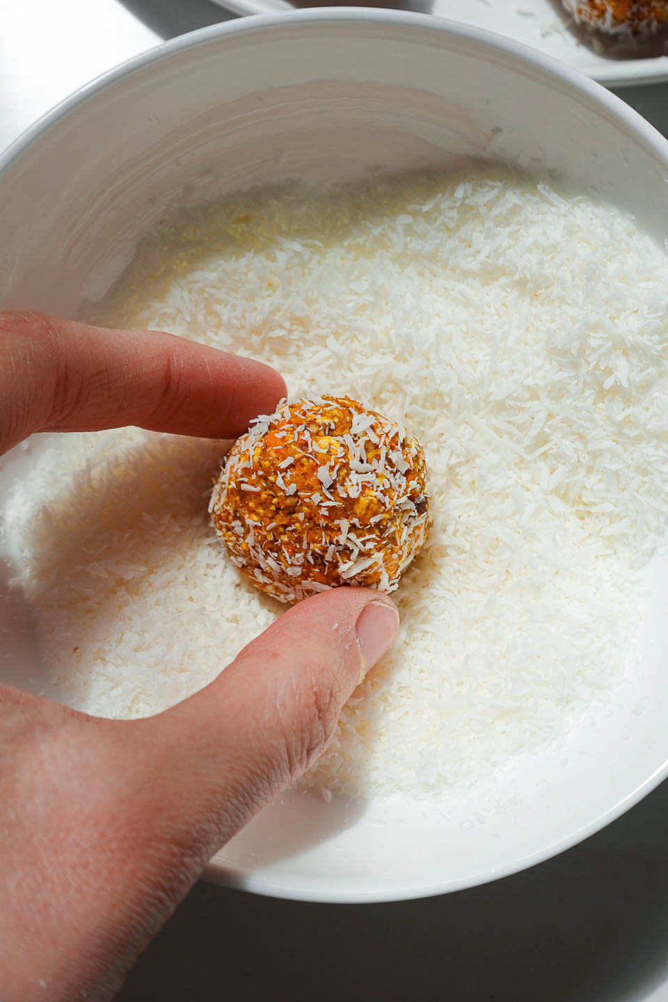 Rolling carrot cake energy balls by hand in shredded coconut