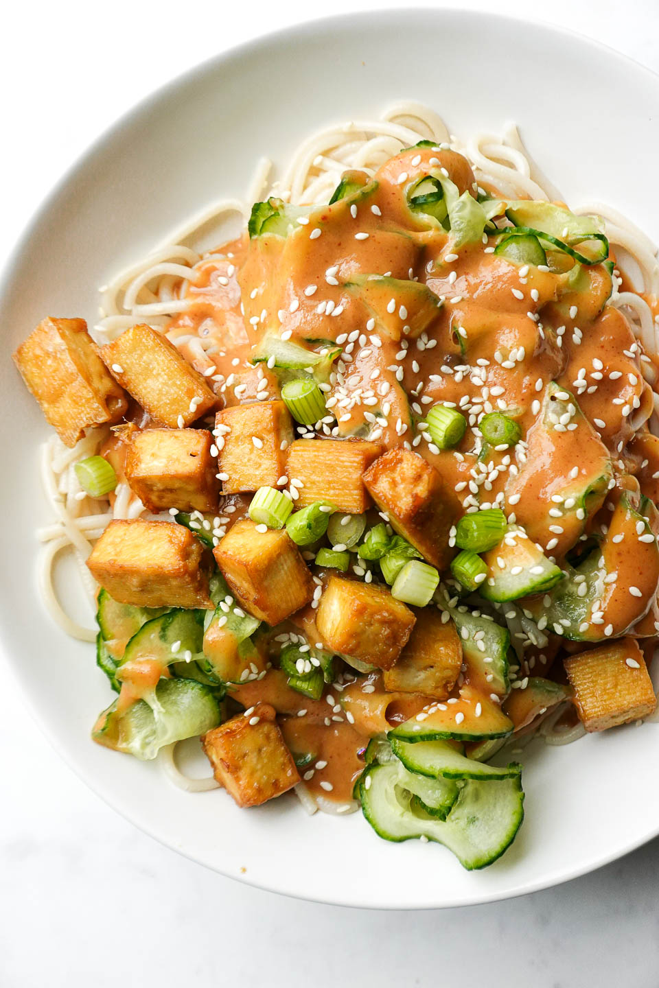 Vegan peanut noodles with tofu and veggies in a white bowl on a marble surface