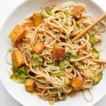 Healthy peanut noodles topped with crispy tofu, spiralized cucumber, scallions, and sesame seeds with chopsticks