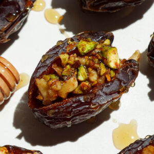 Close-up of a baklava stuffed date showing pistachio and walnut filling inside a soft medjool date with a drizzle of honey
