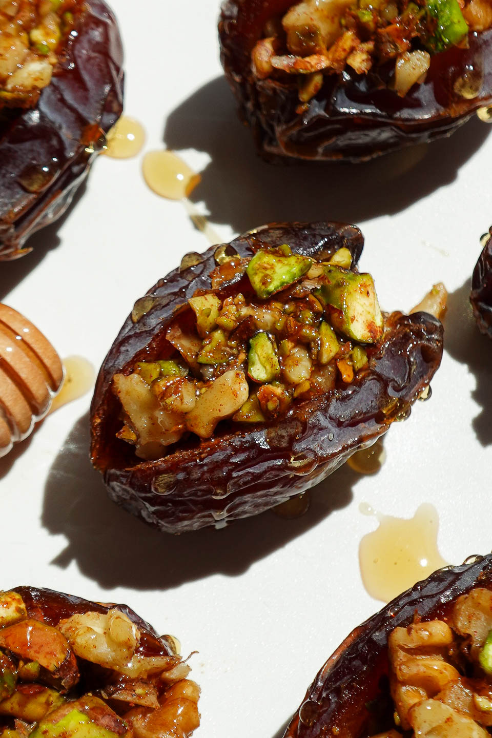 Close-up of a baklava stuffed date showing pistachio and walnut filling inside a soft medjool date with a drizzle of honey