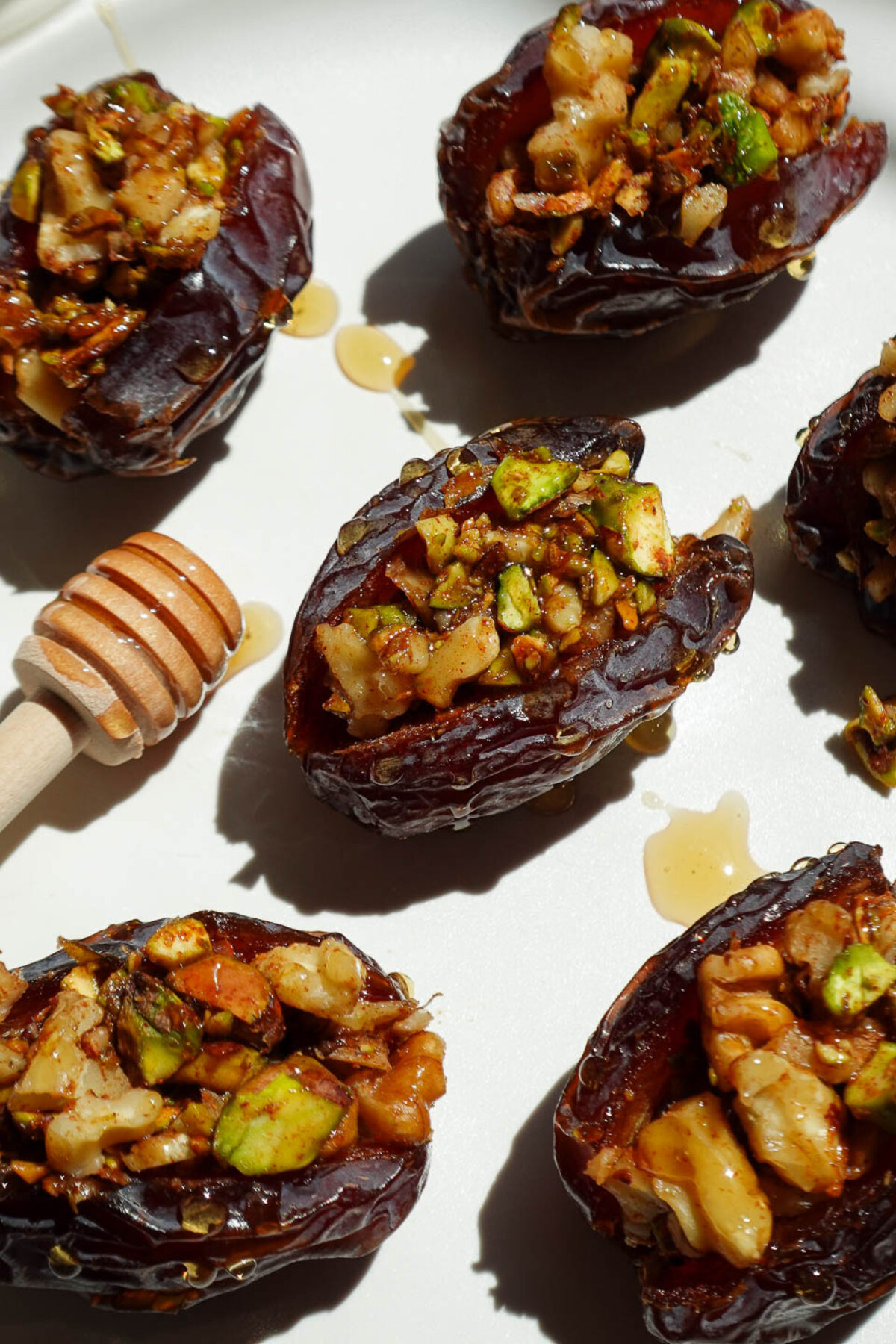 Baklava stuffed medjool dates filled with pistachios, walnuts, and cinnamon arranged on a white plate.