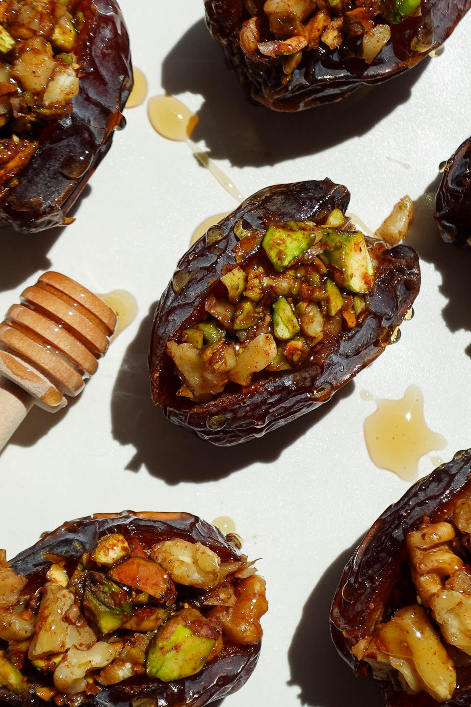 Baklava stuffed dates filled with pistachios, walnuts, and cinnamon arranged on a white plate.