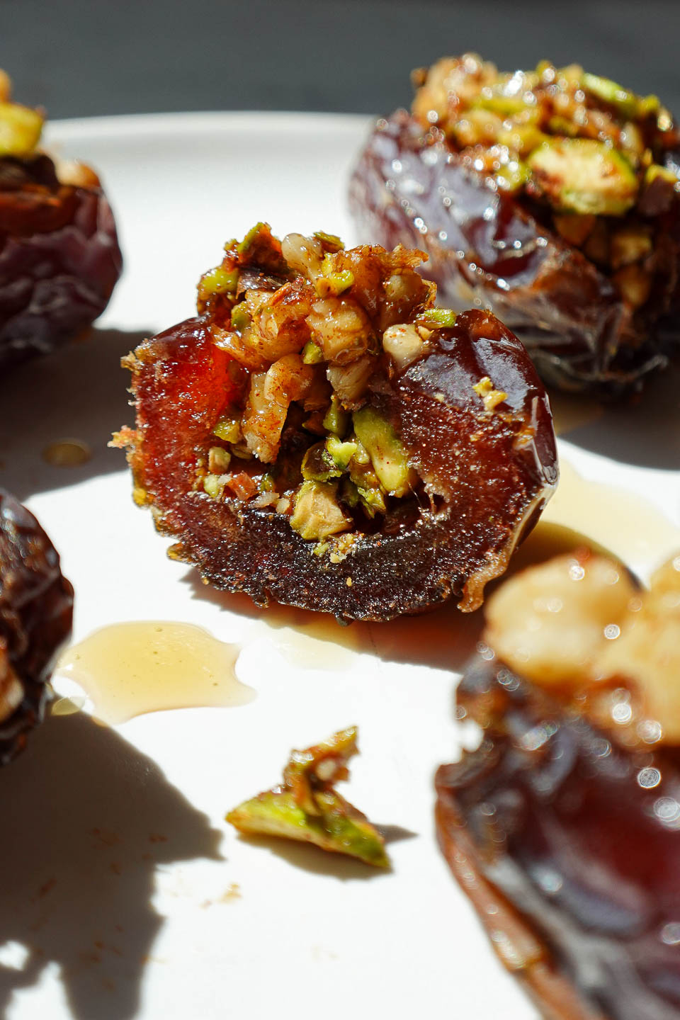Close-up of a baklava stuffed date with a bite taken out of it, showing the pistachio and walnut filling inside a soft medjool date