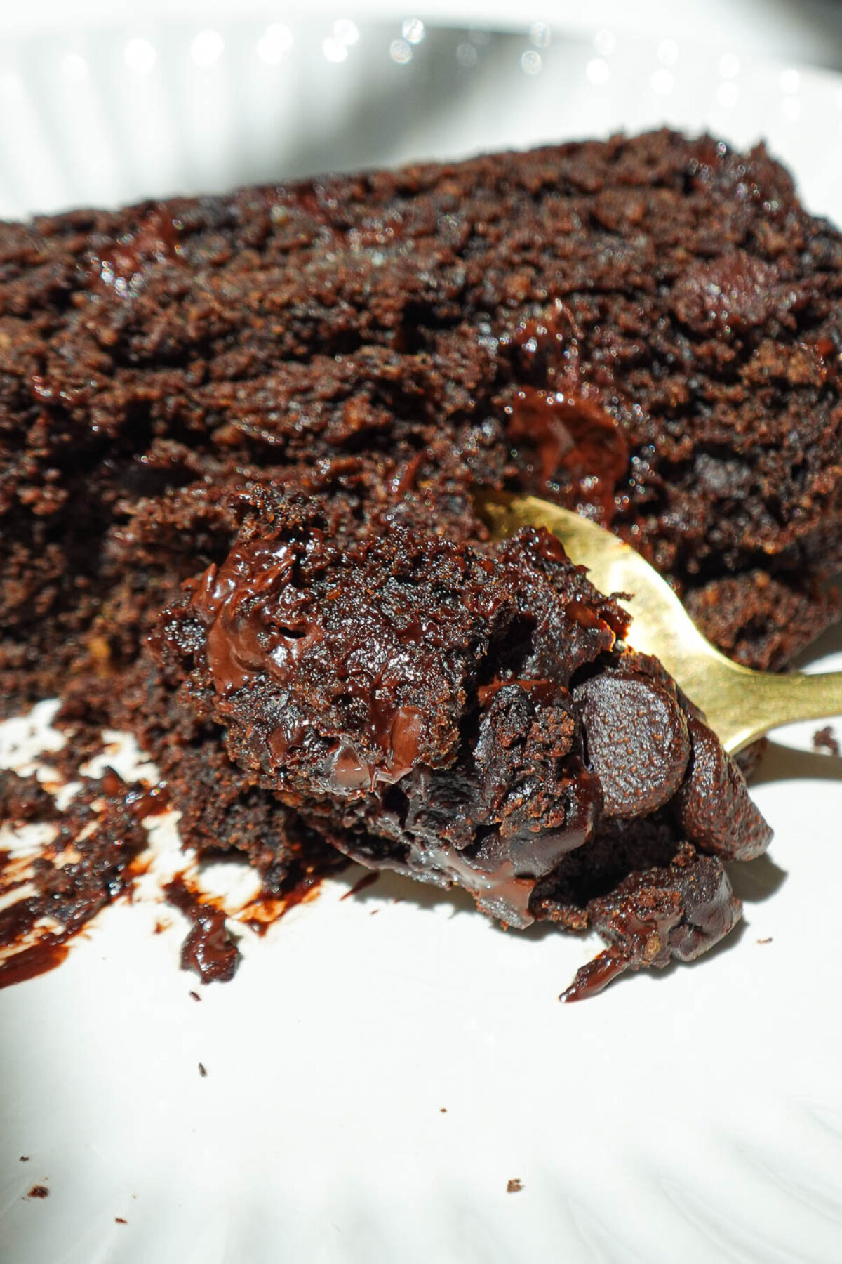 Slice of healthy chocolate banana bread on a plate with a spoon, showing the soft inside and melty chocolate chips.