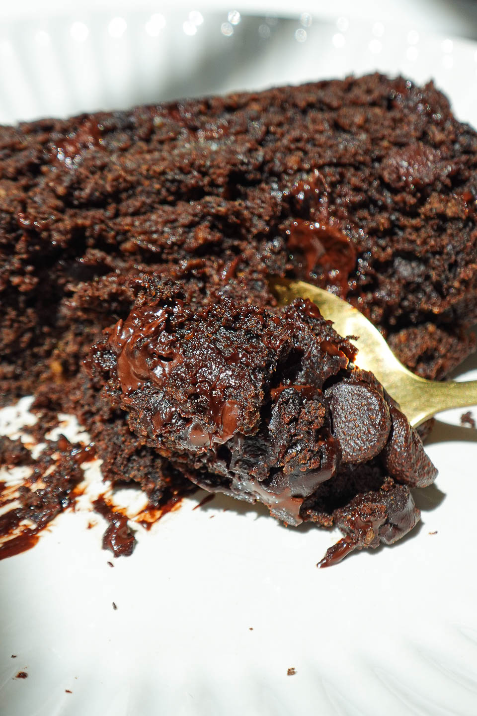 Slice of healthy chocolate banana bread on a plate with a spoon, showing the soft inside and melty chocolate chips.