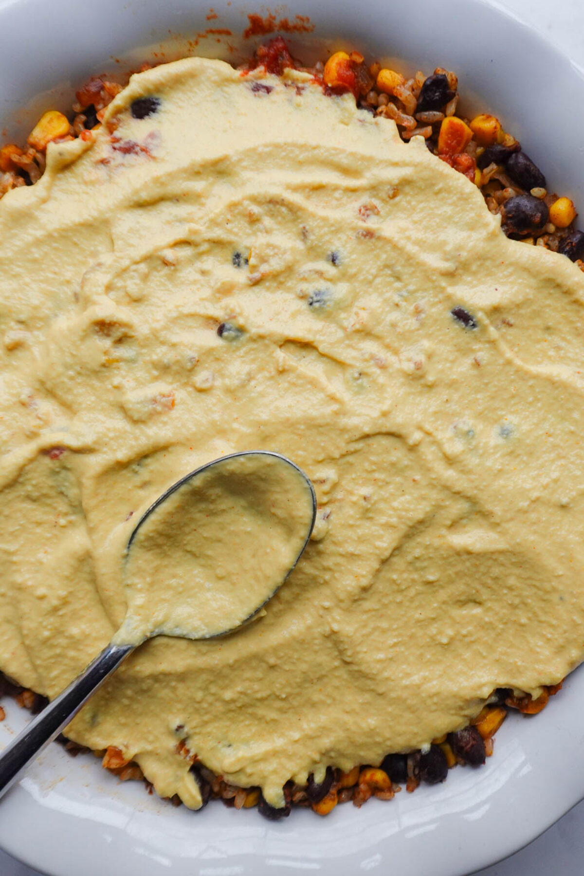 Vegan queso being poured over the assembled casserole