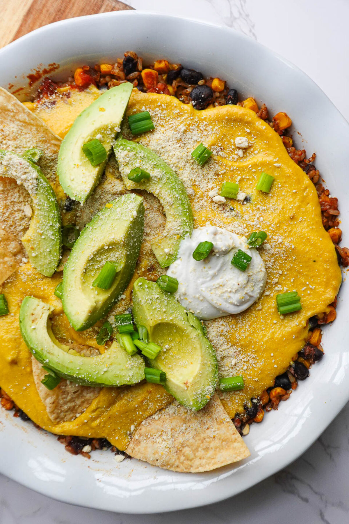 Overhead shot of vegan Mexican rice casserole in a baking dish topped with avocado slices, vegan sour cream, tortilla chips, and scallions