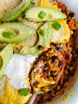 Close-up of a spoon scooping out casserole showing layers of rice, beans, corn, salsa, and creamy vegan queso