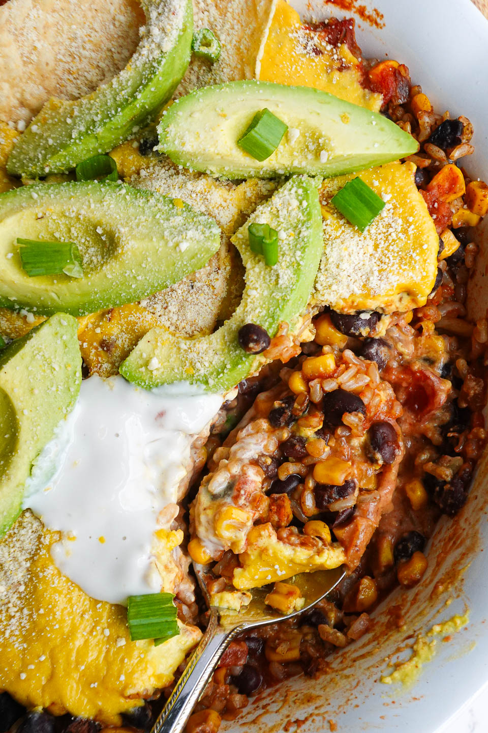 Close-up of a spoon scooping out casserole showing layers of rice, beans, corn, salsa, and creamy vegan queso