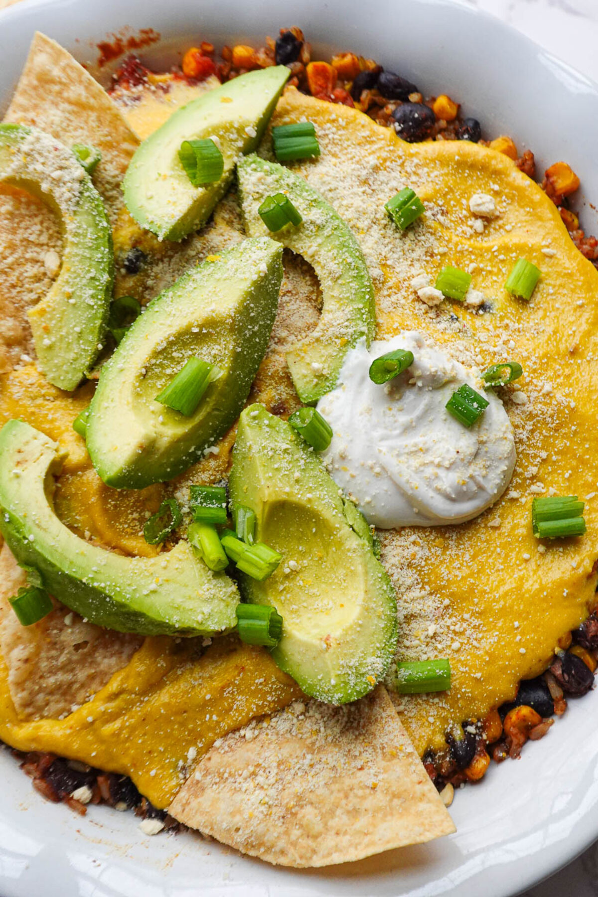 Vegan Mexican casserole topped with avocado slices, vegan sour cream, sliced scallions, tortilla chips.