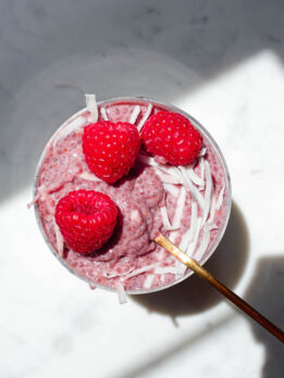 jar of raspberry chia pudding topped with fresh berries and coconut flakes on a white background