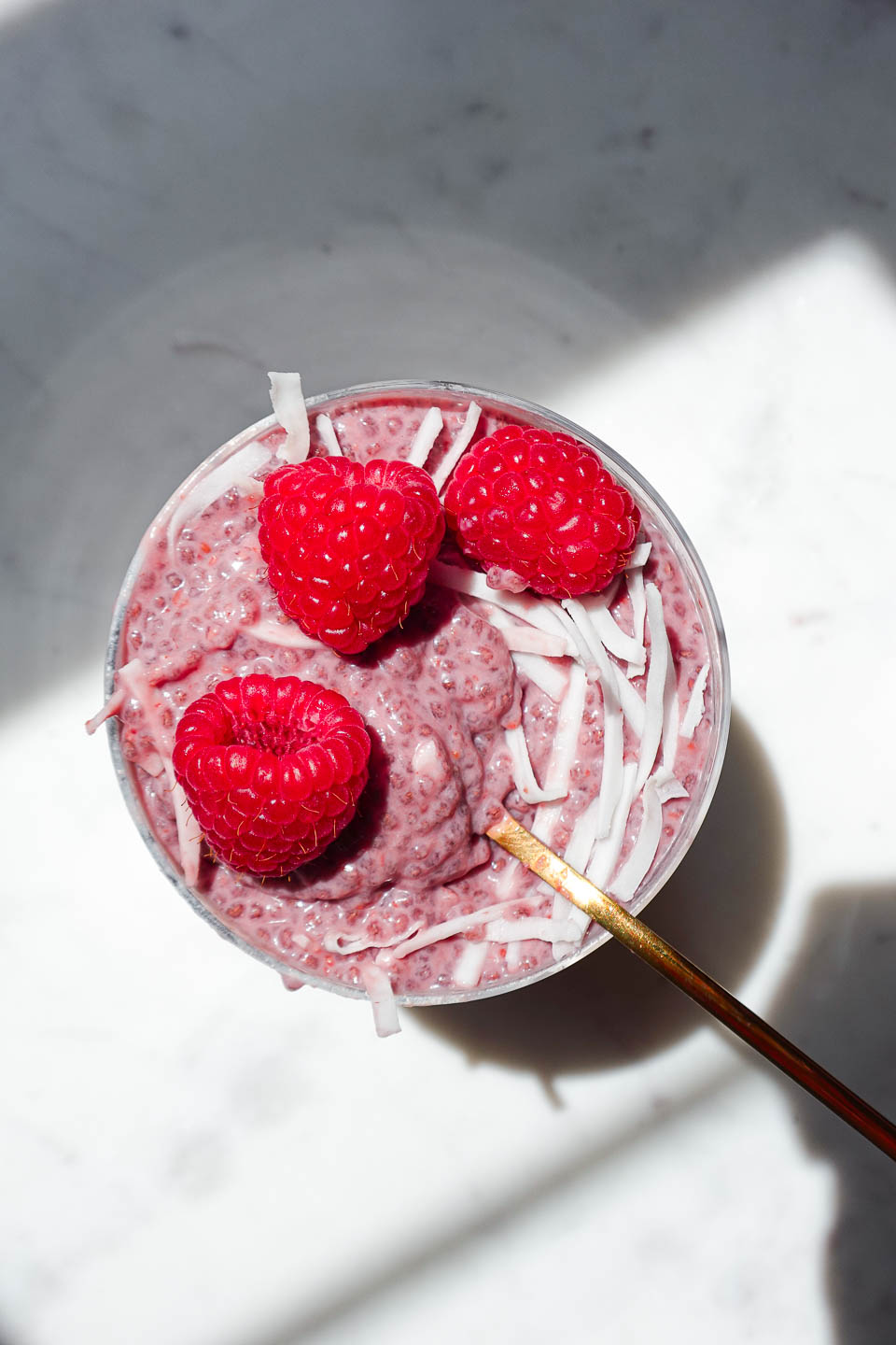 jar of raspberry chia pudding topped with fresh berries and coconut flakes on a white background