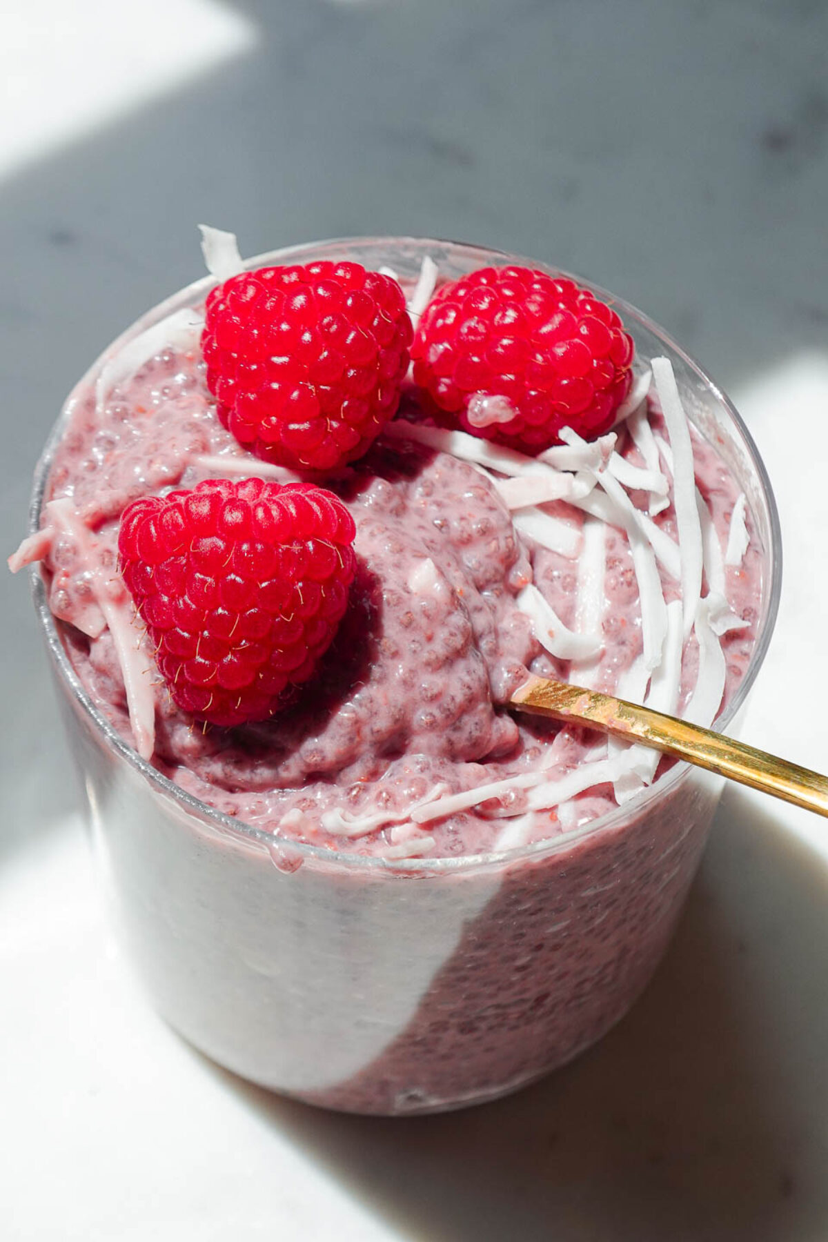 close up of raspberry chia pudding in a glass jar topped with fresh raspberries and coconut flakes