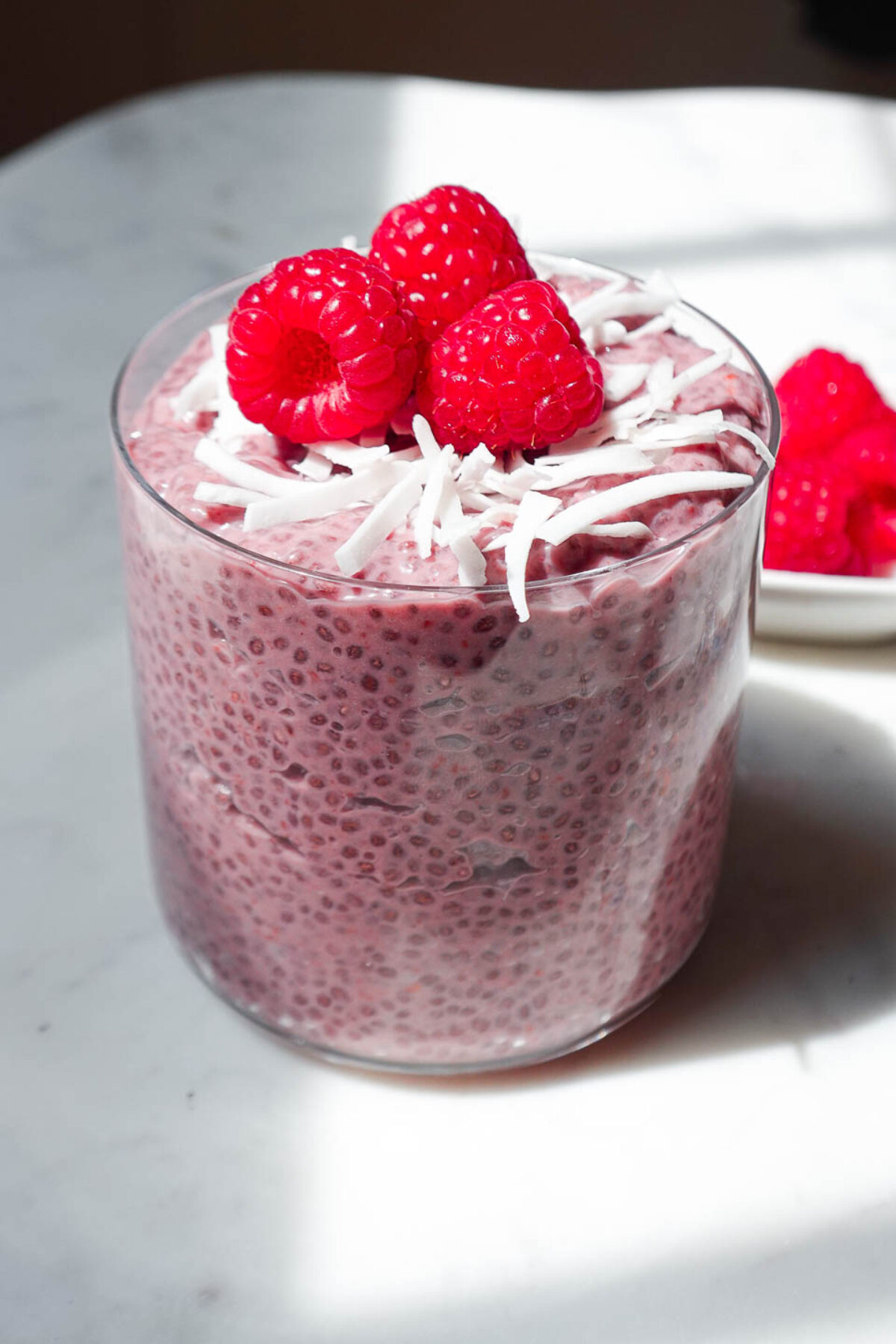 Raspberry chia pudding in a glass jar topped with fresh raspberries and coconut flakes