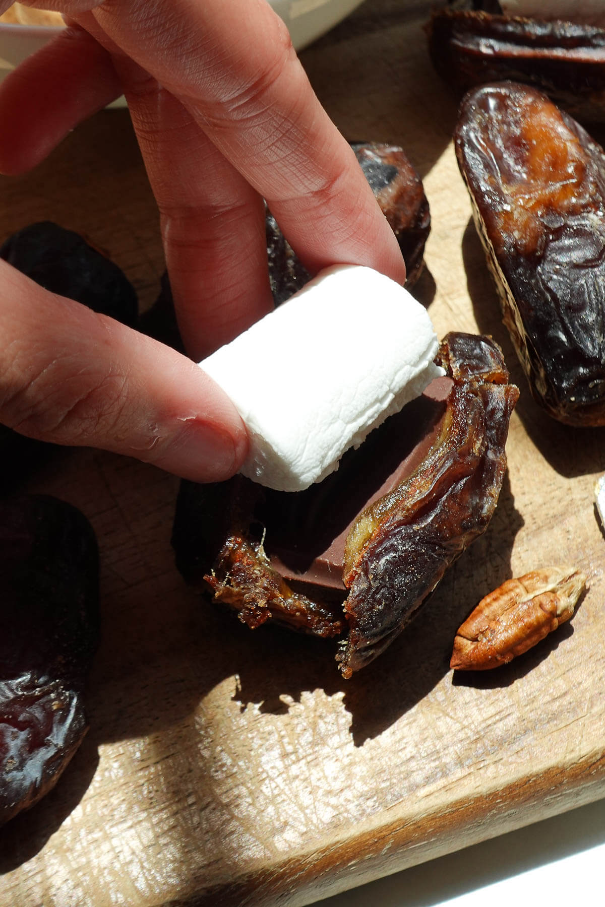 Placing a marshmallow on top of s'mores stuffed dates.