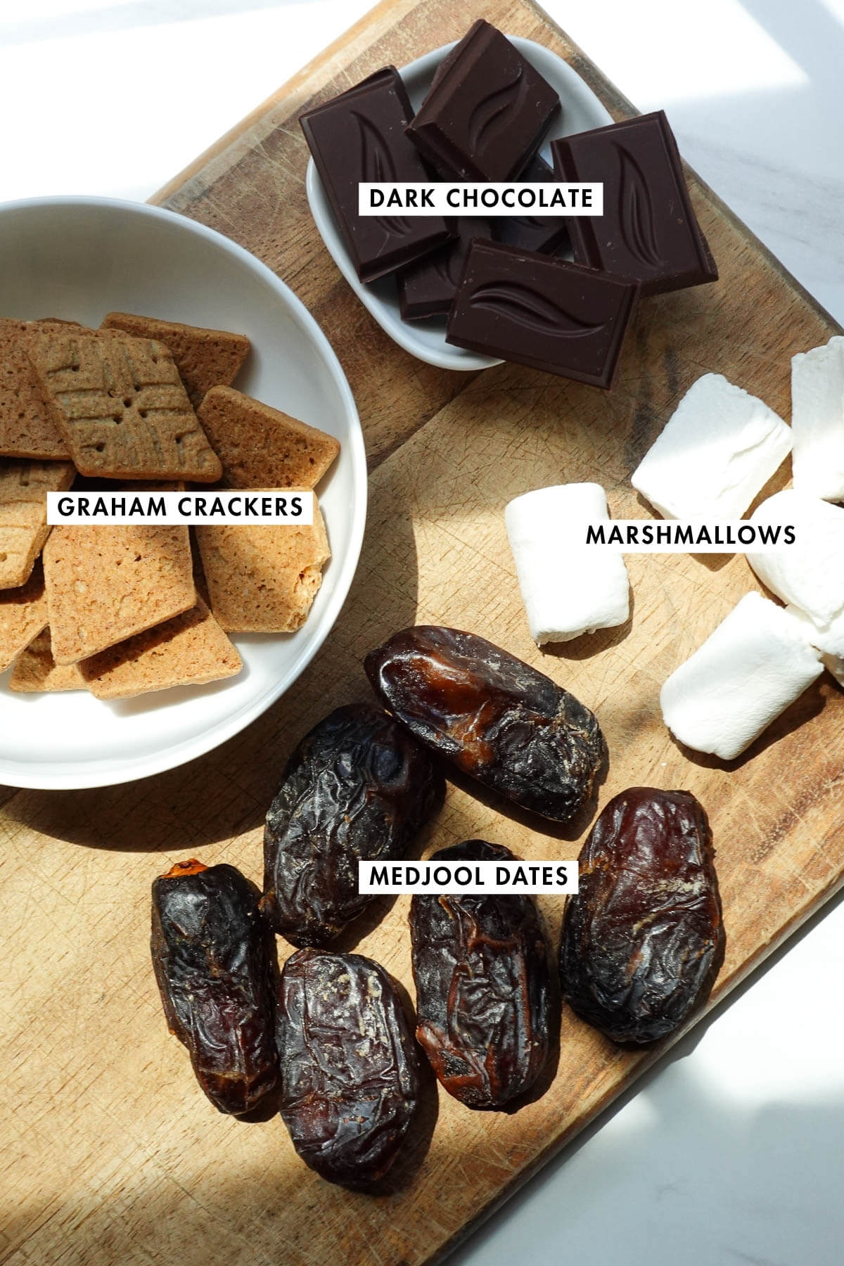 Ingredients to make s'mores stuffed dates on a wood board.