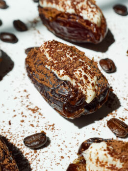 Tiramisu stuffed Medjool dates topped with cocoa powder, arranged on a white plate.