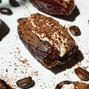 Tiramisu stuffed Medjool dates topped with cocoa powder, arranged on a white plate.