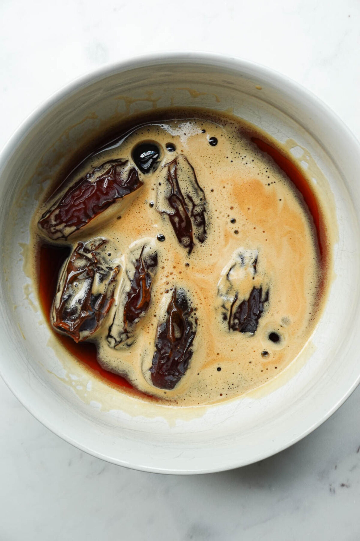 Medjool dates soaking in a bowl of black coffee to absorb tiramisu flavor.
