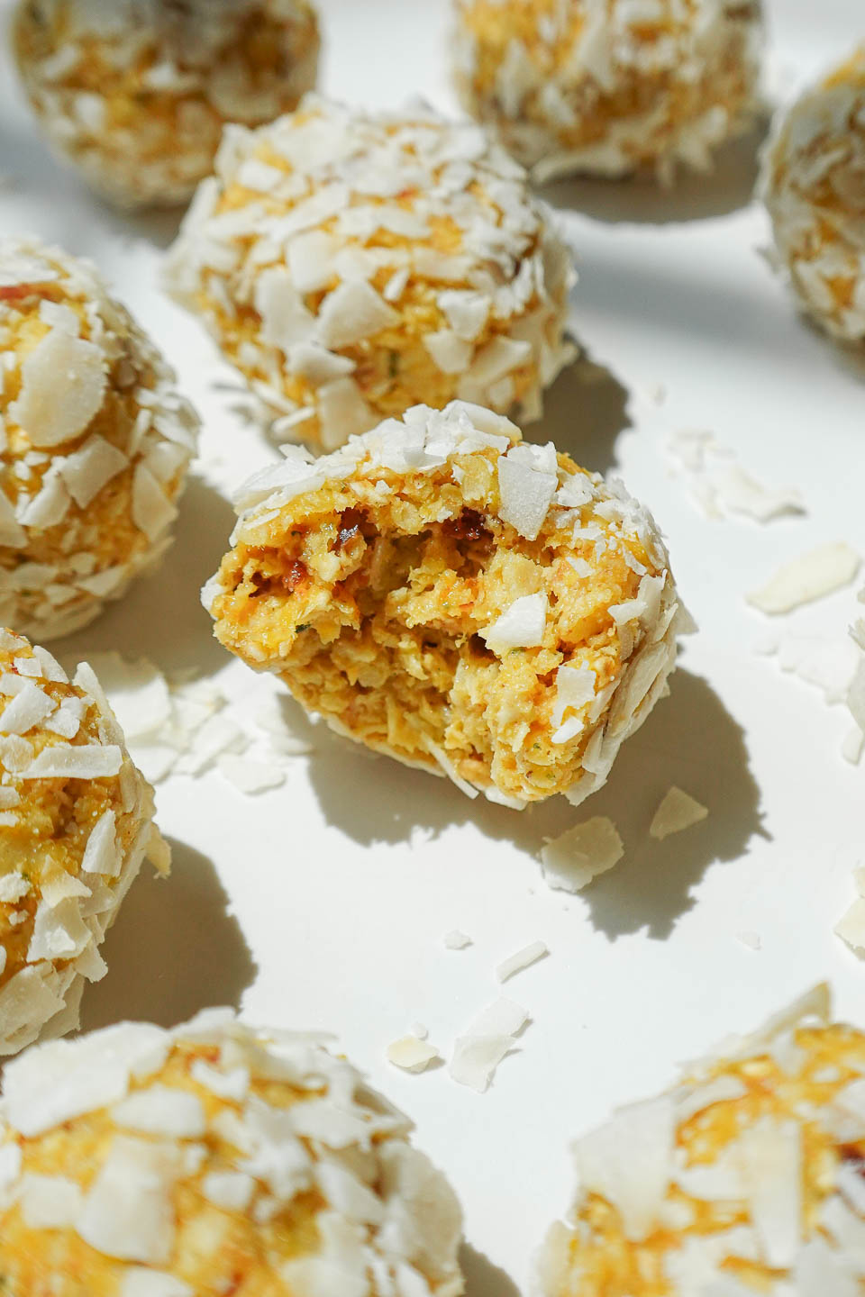Close-up of a mango bliss ball with a chewy, coconut-covered texture.