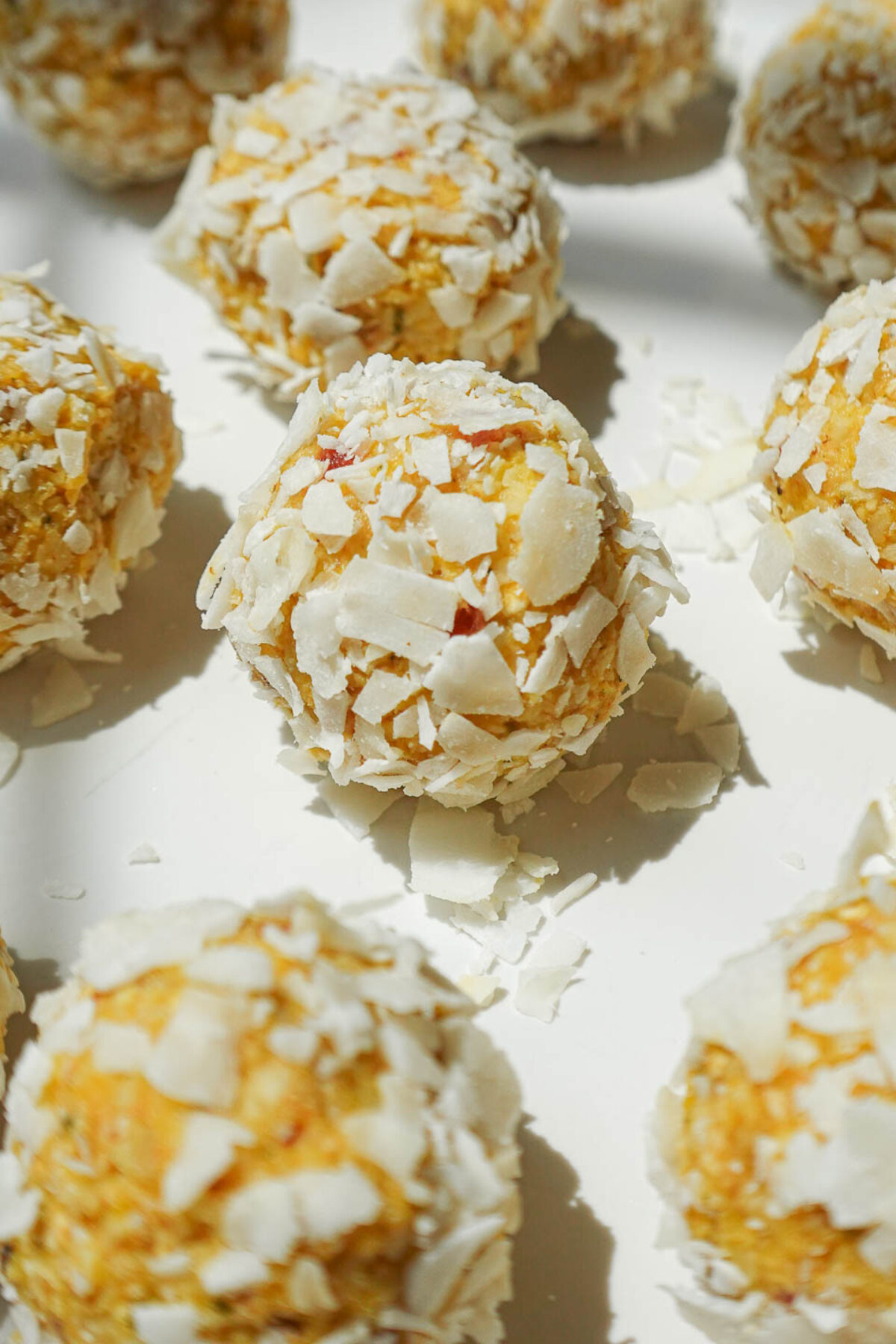 A plate of no-bake mango bliss balls rolled in shredded coconut, arranged on a white plate.