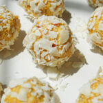 A plate of no-bake mango bliss balls rolled in shredded coconut, arranged on a white plate.