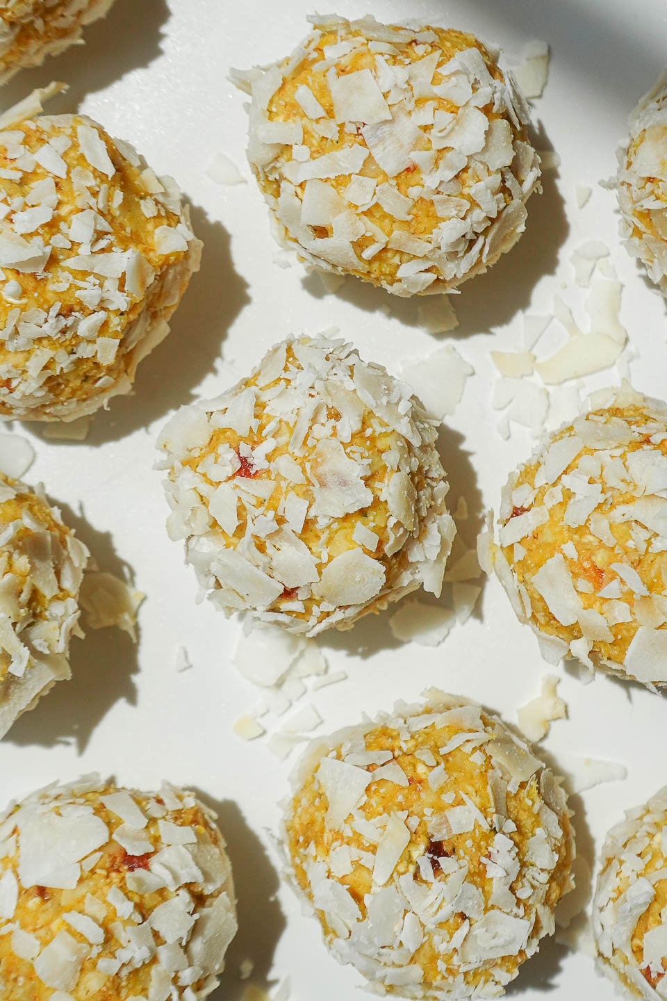 Mango bliss balls being coated in shredded coconut on a plate.