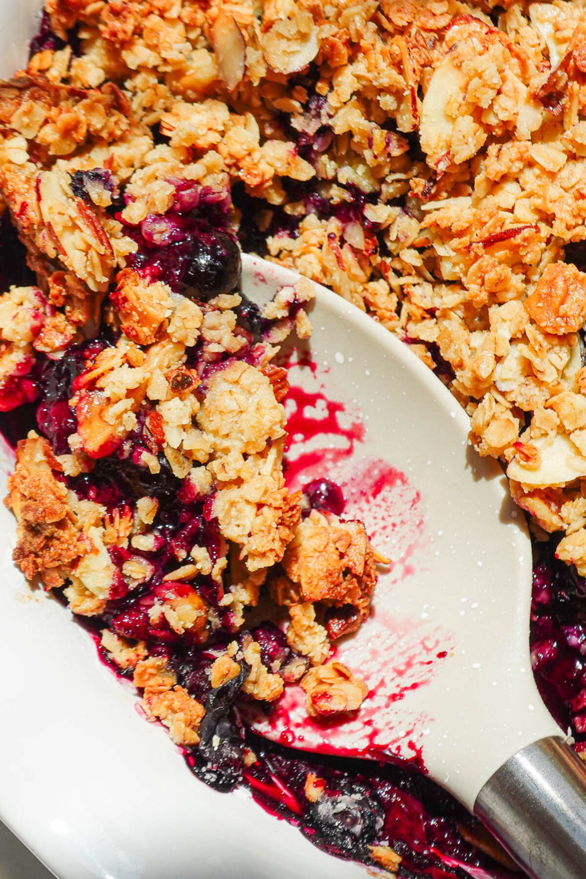 Spoonful of blueberry crisp showing jammy fruit and crumbly almond-oat topping.