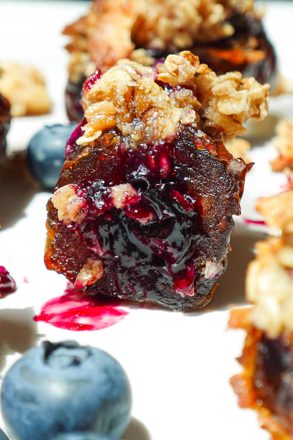 Close-up of a Blueberry Crisp Stuffed Date with a bite taken out, showing gooey blueberry compote and oat topping