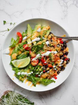Overhead shot of a vegan burrito bowl with brown rice, roasted sweet potatoes, black beans, and fresh toppings in a ceramic bowl