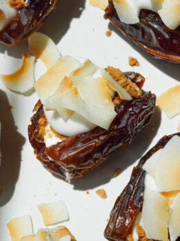 Close-up of creamy coconut cream pie stuffed medjool dates topped with toasted coconut flakes and crushed graham crackers on a white plate.